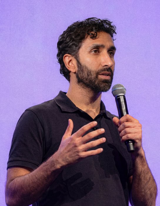 Manick Bhan delivering a speech with a microphone at an event.